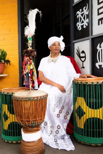 Woman wearing all white sits near three large drums